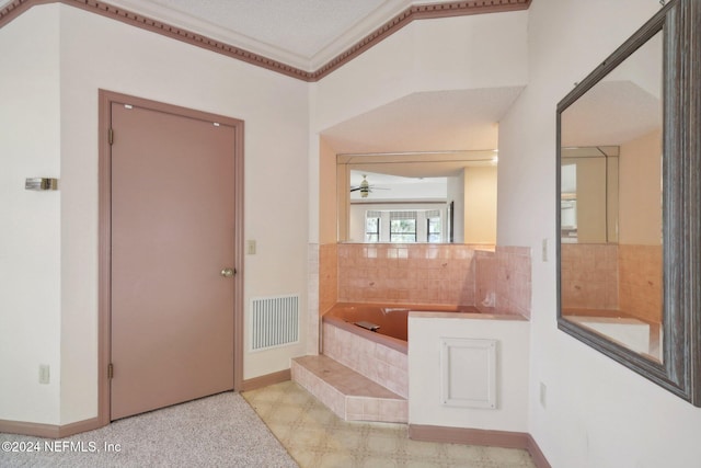 bathroom with a textured ceiling, ceiling fan, and a relaxing tiled tub