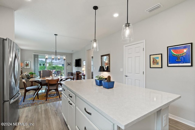 kitchen with white cabinetry, hanging light fixtures, light hardwood / wood-style flooring, a center island, and stainless steel fridge