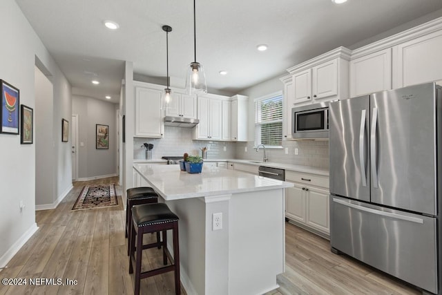 kitchen featuring stainless steel appliances, light hardwood / wood-style floors, a center island, pendant lighting, and white cabinetry