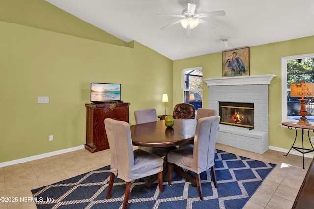 tiled dining space with ceiling fan, lofted ceiling, and a fireplace