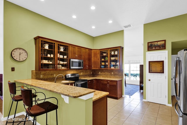 kitchen featuring a breakfast bar area, appliances with stainless steel finishes, kitchen peninsula, light stone countertops, and backsplash