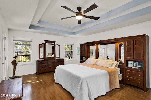 bedroom featuring ceiling fan, dark hardwood / wood-style flooring, a raised ceiling, and a textured ceiling