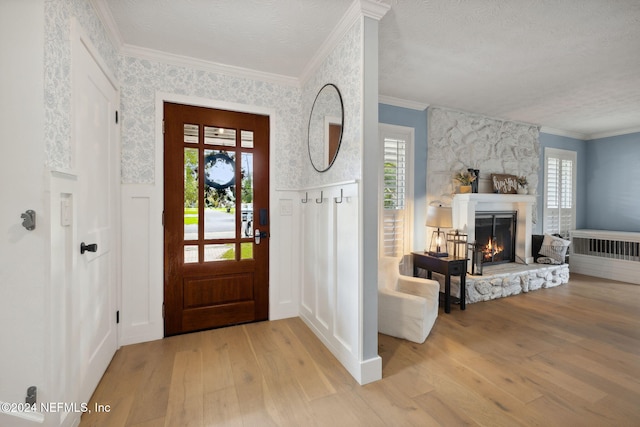 entryway with a textured ceiling, light hardwood / wood-style floors, ornamental molding, and a fireplace