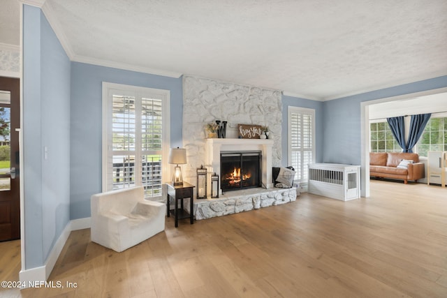 living room featuring hardwood / wood-style flooring, a stone fireplace, ornamental molding, and a textured ceiling