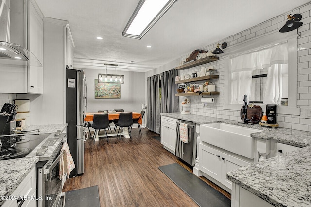 kitchen featuring dark hardwood / wood-style flooring, wall chimney exhaust hood, hanging light fixtures, white cabinetry, and appliances with stainless steel finishes