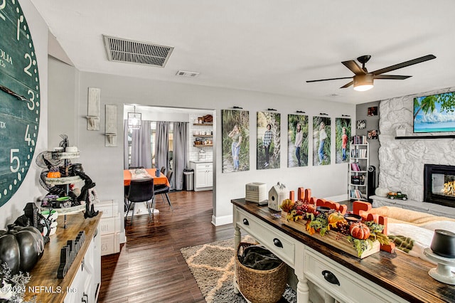 living room featuring dark wood-type flooring, ceiling fan, and a fireplace