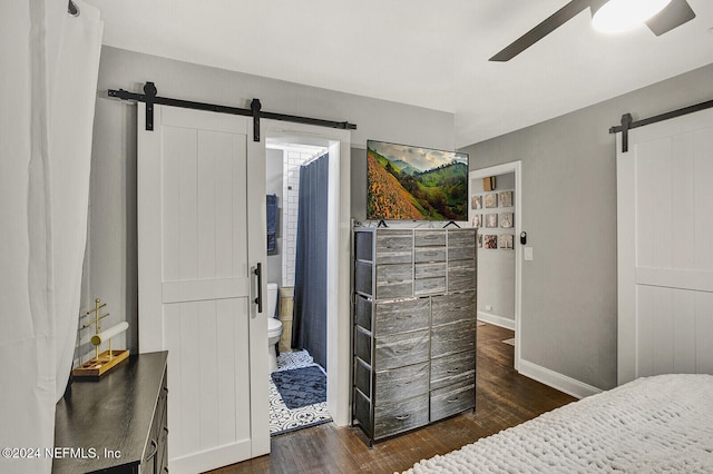 bedroom featuring a barn door, dark hardwood / wood-style floors, ceiling fan, and connected bathroom