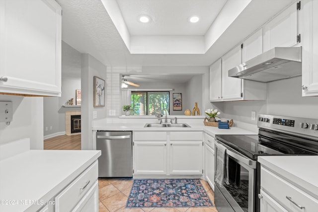 kitchen featuring stainless steel appliances, extractor fan, light tile patterned floors, a fireplace, and white cabinetry