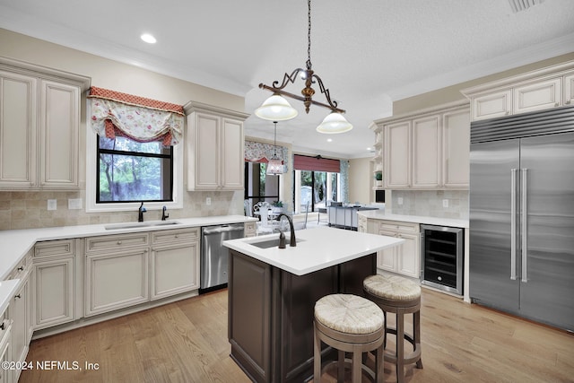 kitchen featuring backsplash, stainless steel appliances, sink, a center island with sink, and wine cooler