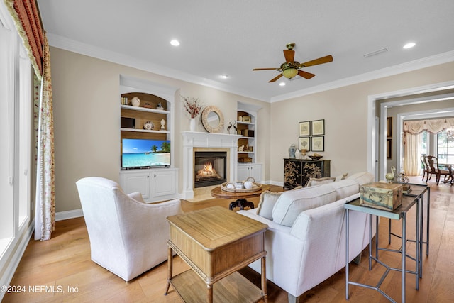 living room featuring ceiling fan, built in features, light hardwood / wood-style floors, and ornamental molding