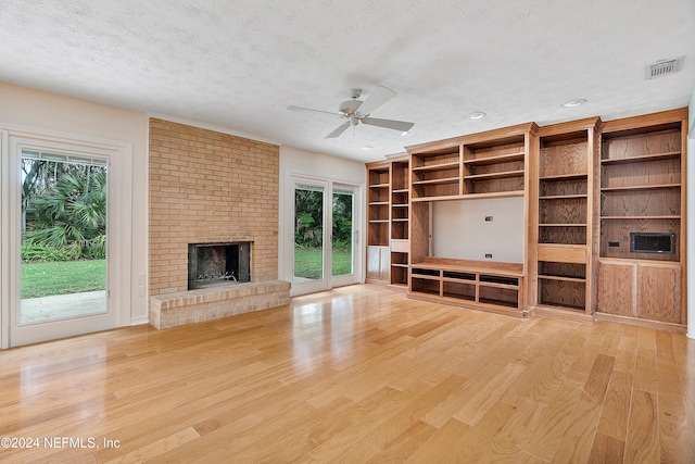 unfurnished living room featuring a brick fireplace, light hardwood / wood-style floors, a textured ceiling, and ceiling fan