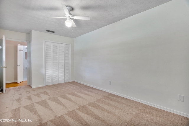 unfurnished bedroom with a closet, a textured ceiling, light carpet, and ceiling fan