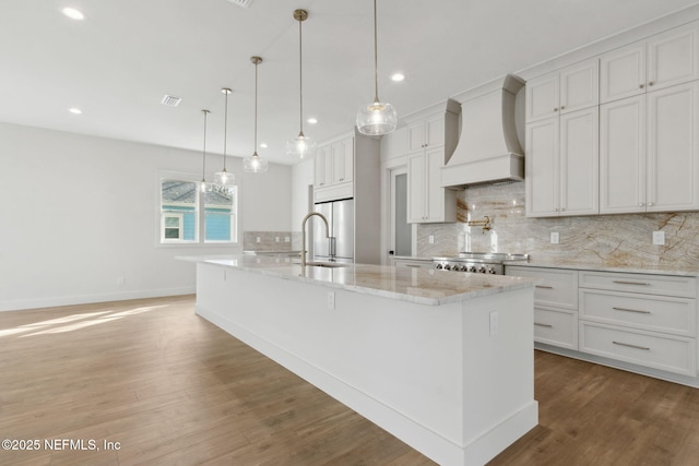 kitchen featuring custom exhaust hood, light wood-style flooring, a sink, decorative backsplash, and stove