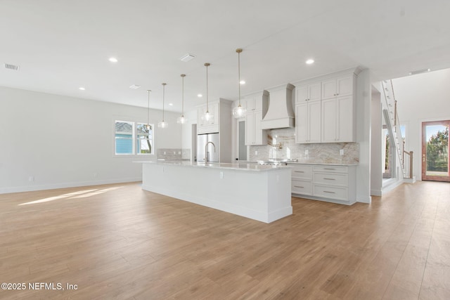 kitchen with custom exhaust hood, light wood-type flooring, tasteful backsplash, and stainless steel refrigerator