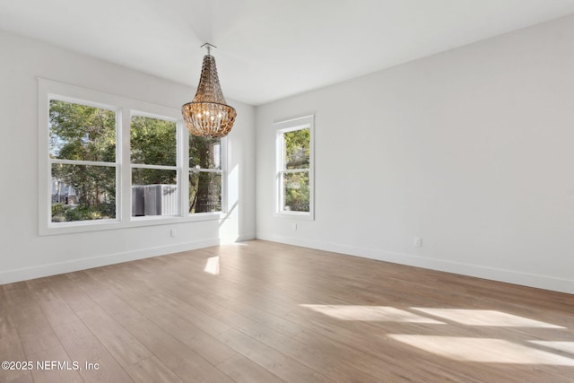 empty room featuring baseboards, an inviting chandelier, and wood finished floors