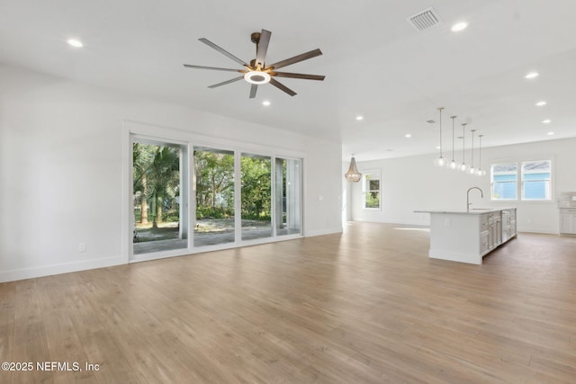 unfurnished living room featuring baseboards, recessed lighting, light wood-style flooring, a ceiling fan, and a sink