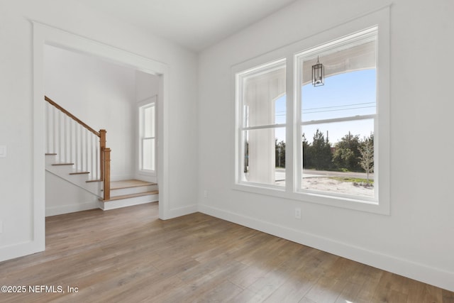 empty room featuring stairway, a healthy amount of sunlight, baseboards, and light wood finished floors