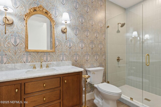 bathroom with vanity, baseboards, wallpapered walls, a shower stall, and toilet