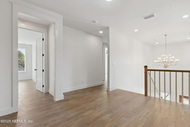 empty room with visible vents, a notable chandelier, wood finished floors, recessed lighting, and baseboards