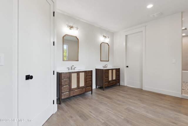 full bath with visible vents, two vanities, a sink, wood finished floors, and baseboards