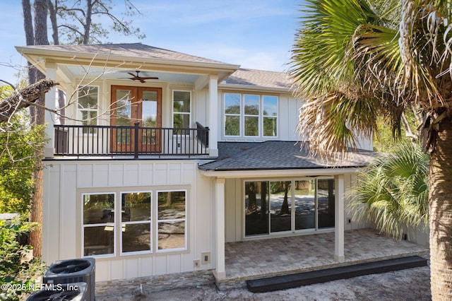 rear view of property with central air condition unit, board and batten siding, a shingled roof, a balcony, and a patio area