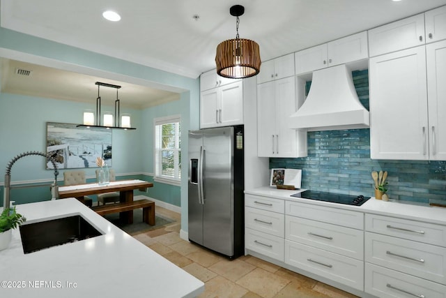 kitchen featuring a sink, light countertops, custom range hood, stainless steel refrigerator with ice dispenser, and black electric stovetop