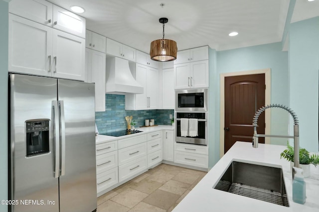 kitchen with tasteful backsplash, premium range hood, stone tile floors, stainless steel appliances, and a sink