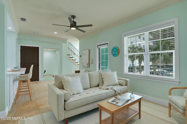 living area featuring stairway, a ceiling fan, visible vents, baseboards, and ornamental molding