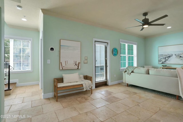 living room with baseboards, a ceiling fan, stone tile floors, and crown molding