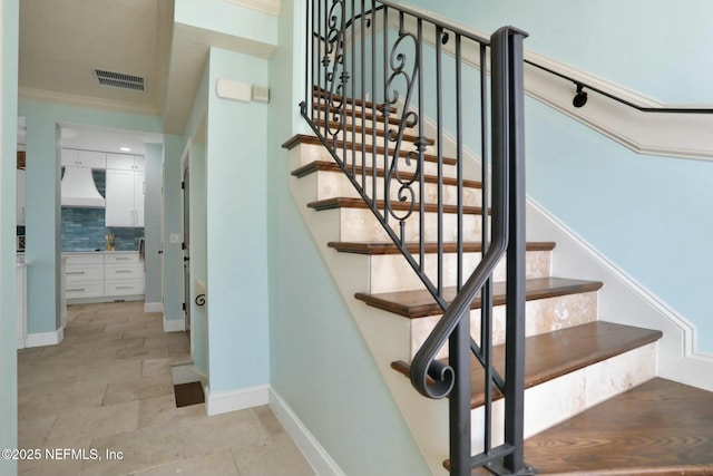 stairway with visible vents, stone finish floor, crown molding, and baseboards