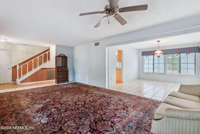 unfurnished living room with ceiling fan, light tile patterned flooring, and a textured ceiling