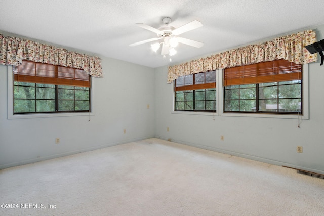 spare room with a textured ceiling, light colored carpet, and ceiling fan