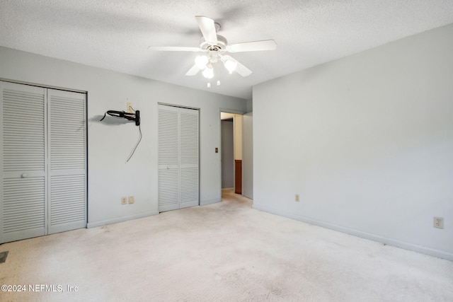 unfurnished bedroom with a textured ceiling, light colored carpet, two closets, and ceiling fan