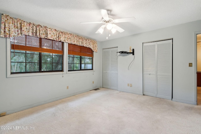 unfurnished bedroom featuring a textured ceiling, light colored carpet, two closets, and ceiling fan