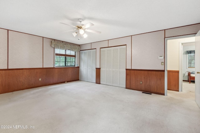 unfurnished bedroom with light carpet, ceiling fan, and wooden walls