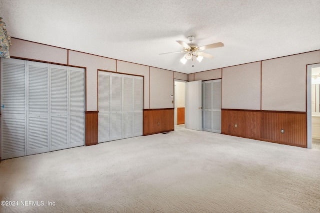 unfurnished bedroom with ceiling fan, two closets, a textured ceiling, and light colored carpet