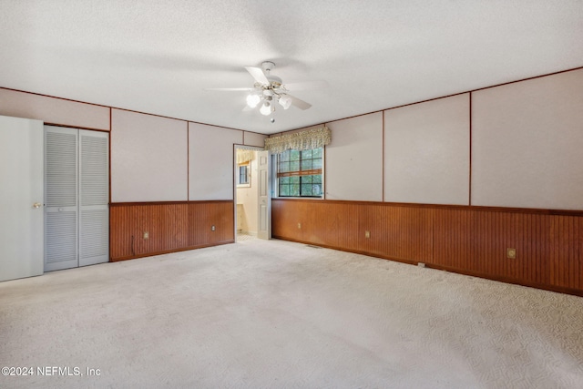 interior space featuring wood walls, a closet, ceiling fan, a textured ceiling, and light carpet