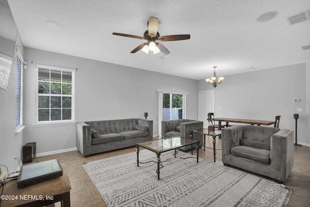 living room featuring baseboards, visible vents, tile patterned flooring, a textured ceiling, and ceiling fan with notable chandelier