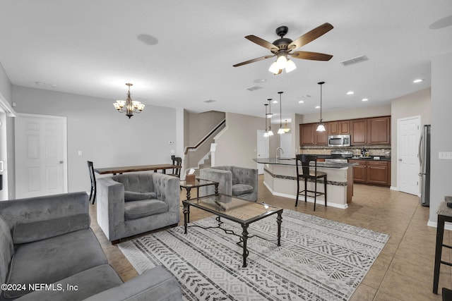 living area with light tile patterned floors, ceiling fan with notable chandelier, visible vents, baseboards, and stairway