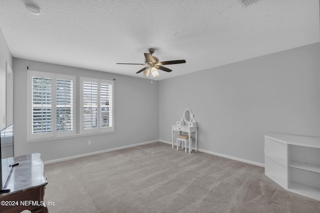 carpeted empty room with a ceiling fan, baseboards, and a textured ceiling