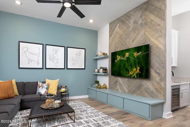 living room featuring a textured ceiling, sink, light hardwood / wood-style floors, beverage cooler, and ceiling fan