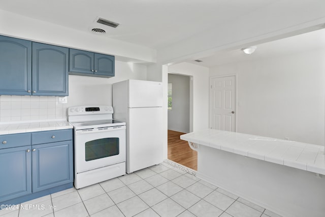 kitchen with white appliances, blue cabinetry, light tile patterned floors, and tile counters