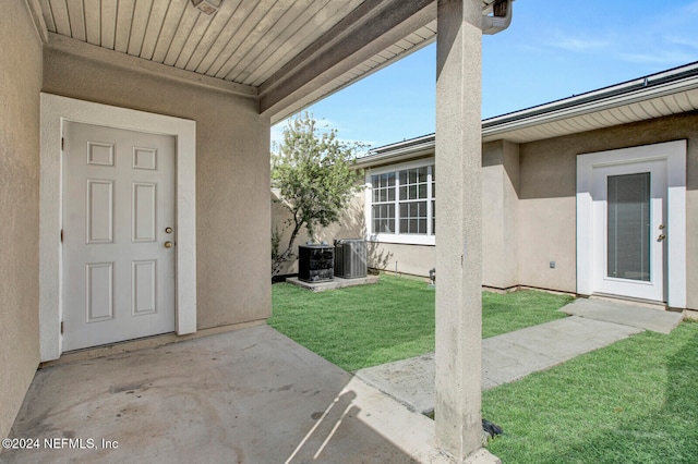 view of exterior entry featuring central AC unit, a yard, and a patio area