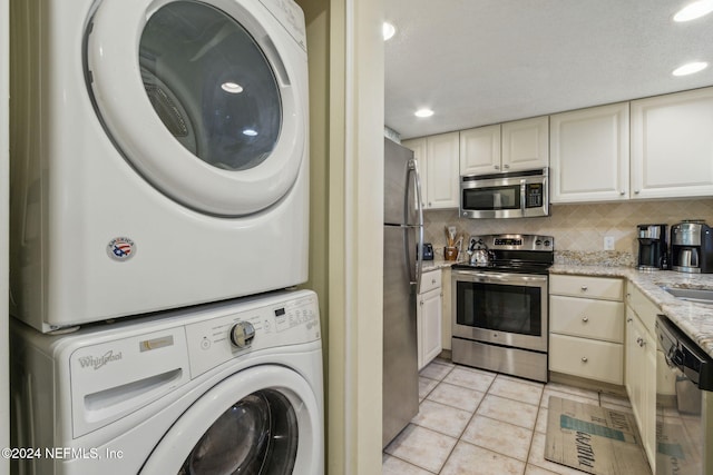 kitchen featuring stacked washing maching and dryer, light stone counters, stainless steel appliances, light tile patterned floors, and decorative backsplash