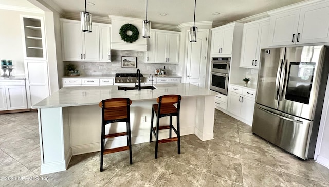 kitchen with a kitchen island with sink, hanging light fixtures, decorative backsplash, white cabinetry, and stainless steel appliances