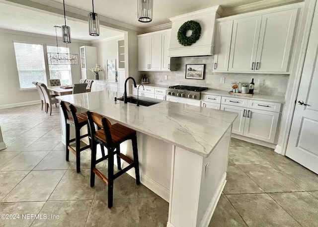 kitchen featuring stainless steel gas stovetop, sink, a center island with sink, white cabinetry, and hanging light fixtures