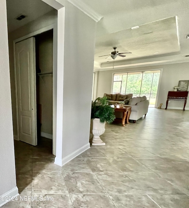 living room featuring a raised ceiling, ceiling fan, and crown molding