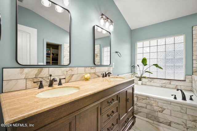 bathroom featuring tiled tub, vanity, and vaulted ceiling