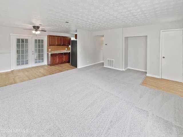 unfurnished living room featuring light wood-type flooring, a textured ceiling, ceiling fan, and french doors