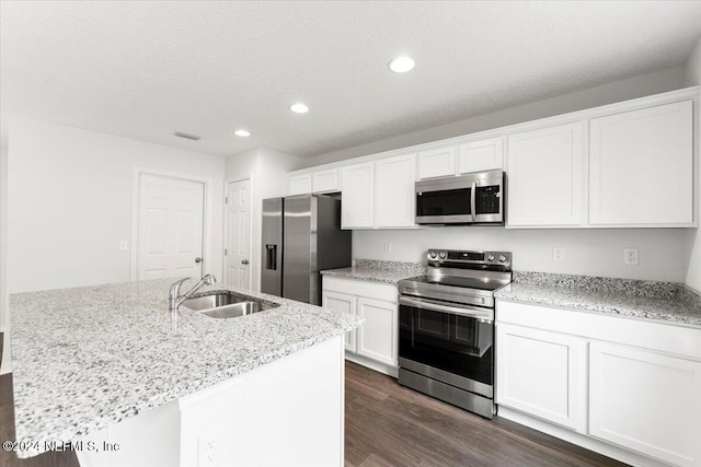 kitchen with light stone counters, stainless steel appliances, dark hardwood / wood-style flooring, white cabinets, and a kitchen island with sink